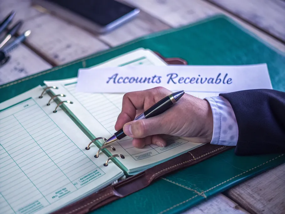 Professional accountant's hand writing in a leather-bound ledger with 'Accounts Receivable' visible.