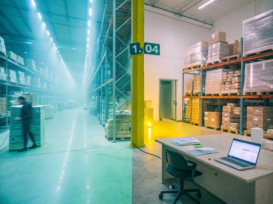 A dramatic modern warehouse interior divided by light, showcasing cluttered inventory on the left and a minimalist desk with financial data on the right.