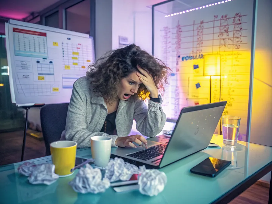 Stressed female entrepreneur overwhelmed by financial spreadsheets in a modern office.